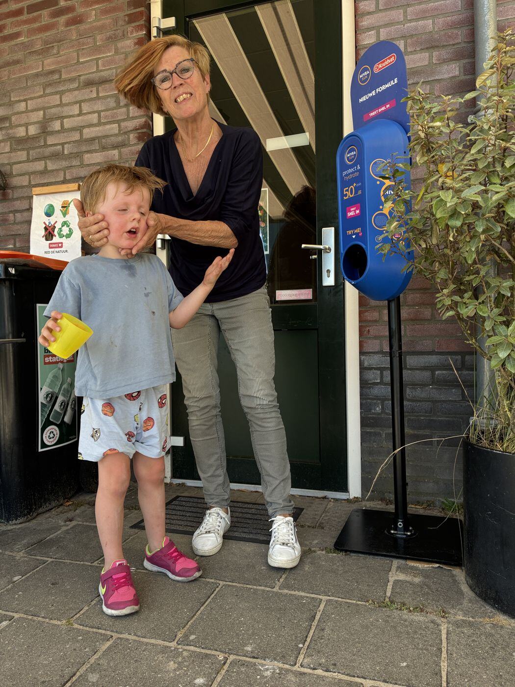 Vrijwilliger en kind bij de zonnebrandautomaat bij de ingang