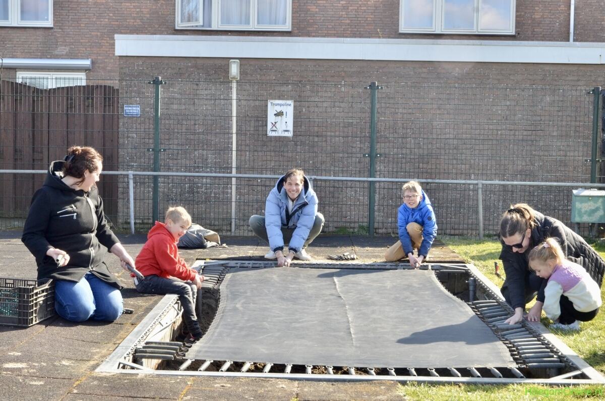 Vrijwilligers en kinderen leggen samen de trampoline aan